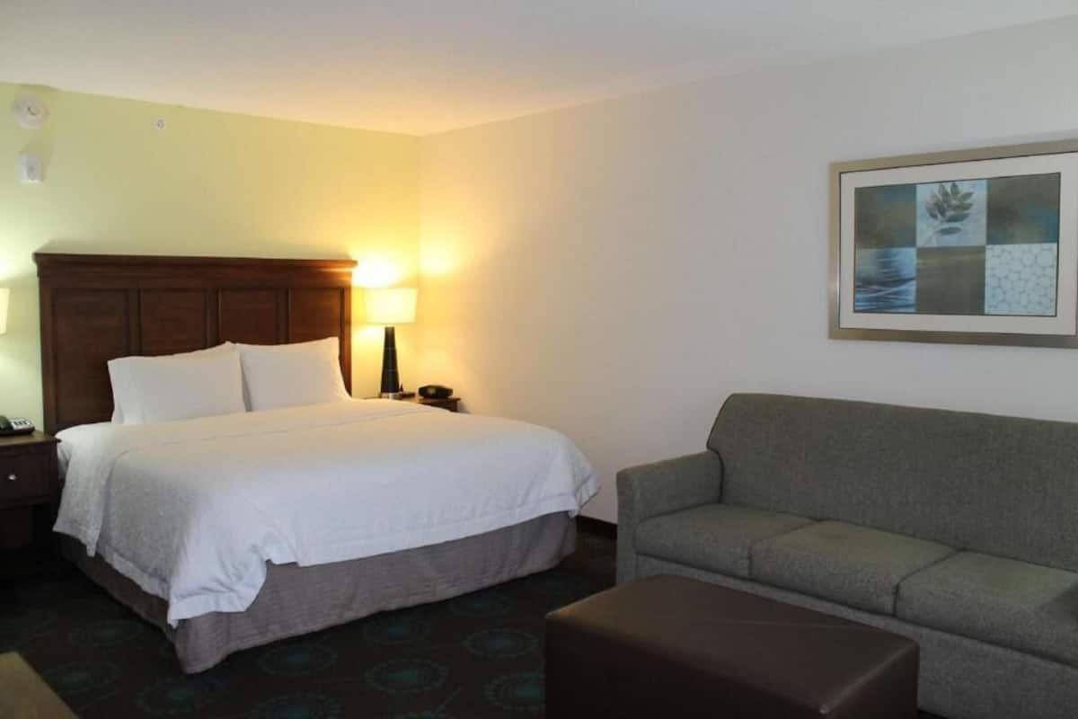 A hotel room with a bed, a bedside table with a lamp, a couch, and a framed picture on the wall.