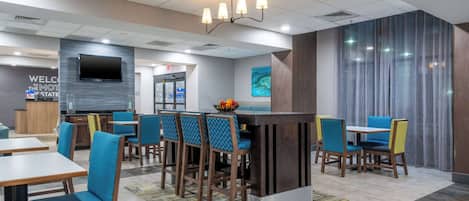 A modern hotel lobby with a reception desk, seating area, and a TV screen.