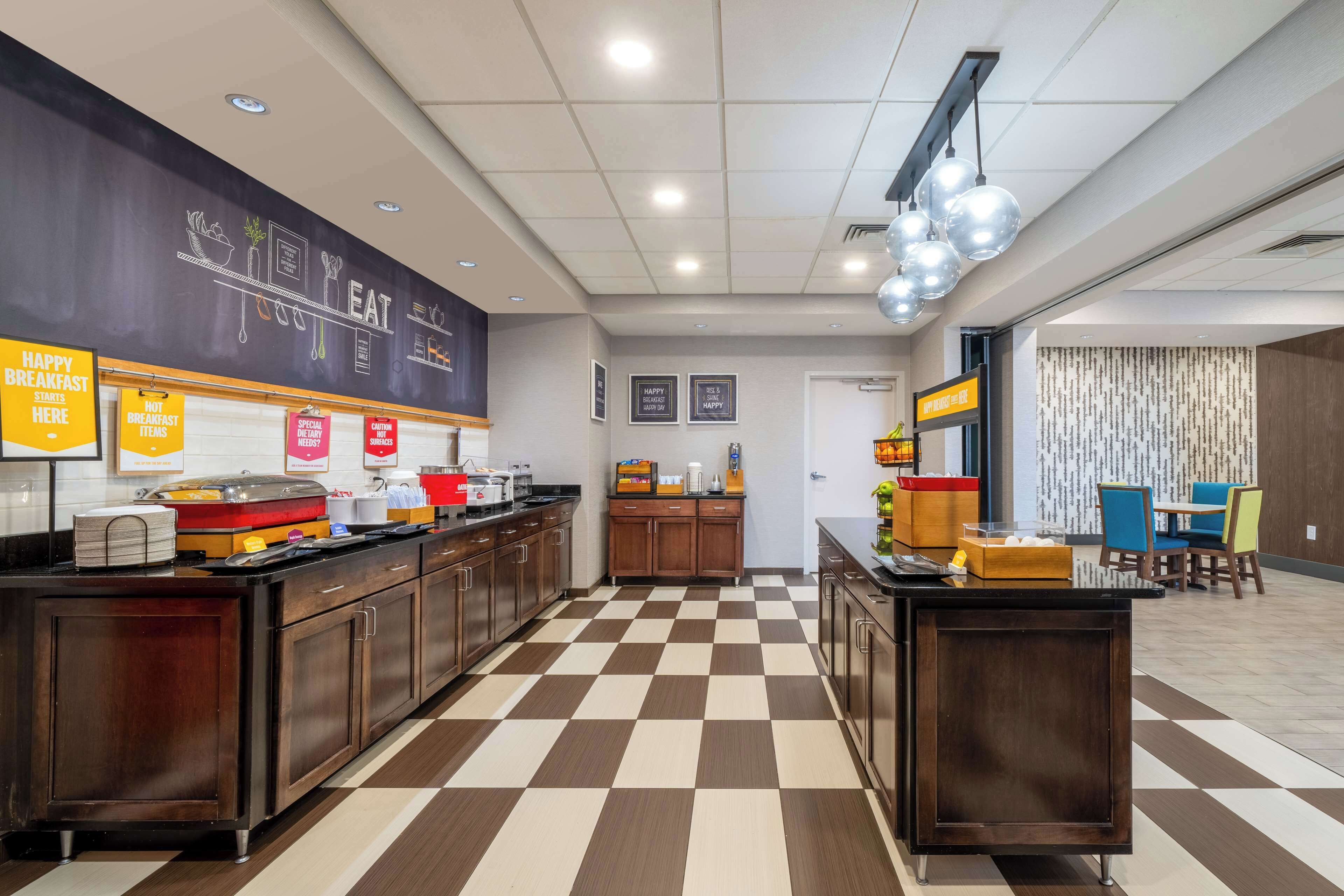 A modern breakfast area with a checkered floor, wooden cabinets, and a counter with various breakfast items.