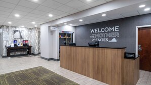 A reception area with a wooden reception desk, a 'Welcome to the Mother of States' sign, a 'Suite Store' sign, and a 'Hilton Honors' sign. - Hampton Inn Dahlgren (King George)