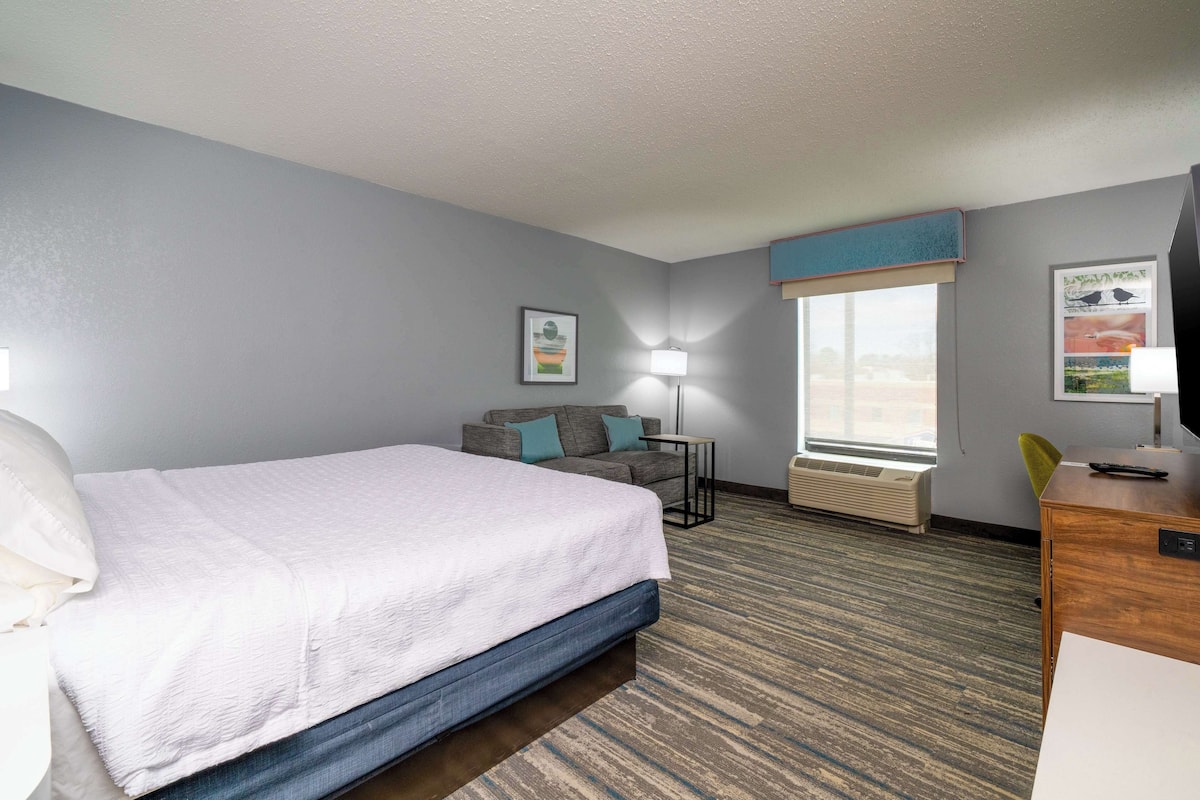 A hotel room with a bed, a sofa, a desk, a lamp, and a window with a view.