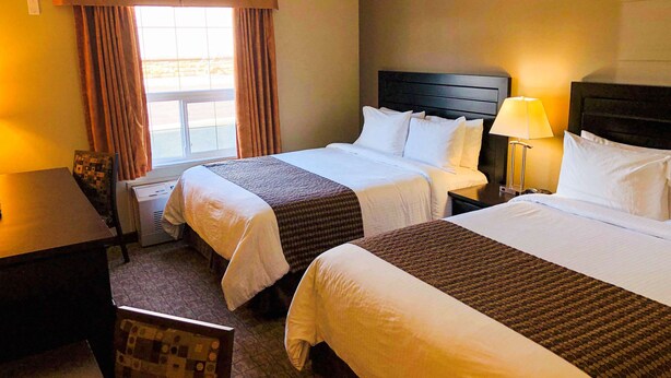 Habitación de hotel con dos camas, un escritorio, una silla y un ventanal con cortinas.