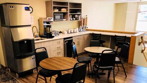 Cocina compacta con refrigerador, microondas y cafetera. Cuenta con gabinetes de madera, un lavamanos y un comedor con mesa y sillas.