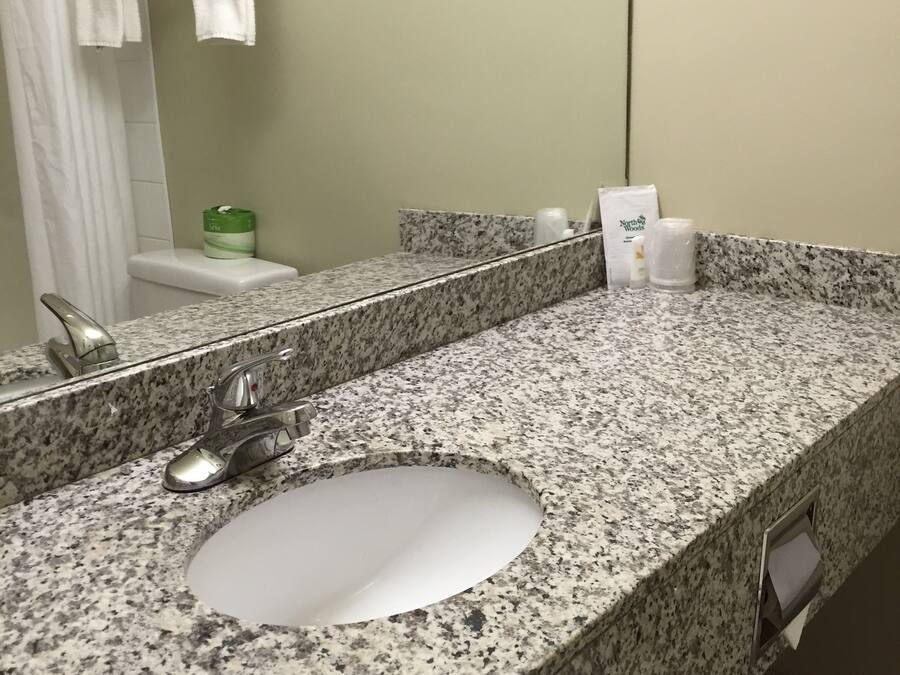 A bathroom with a granite countertop, a sink, a mirror, and a towel rack with folded towels.