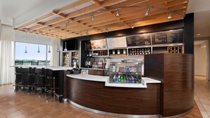Un espace bar moderne avec un plafond en bois, des tabourets de bar, un présentoir réfrigéré et un tableau affichant le menu.