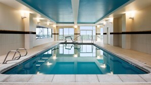 Une piscine intérieure à l’eau d’un bleu limpide, dotée d’un plongeoir et offrant une vue sur le ciel grâce à de grandes fenêtres.