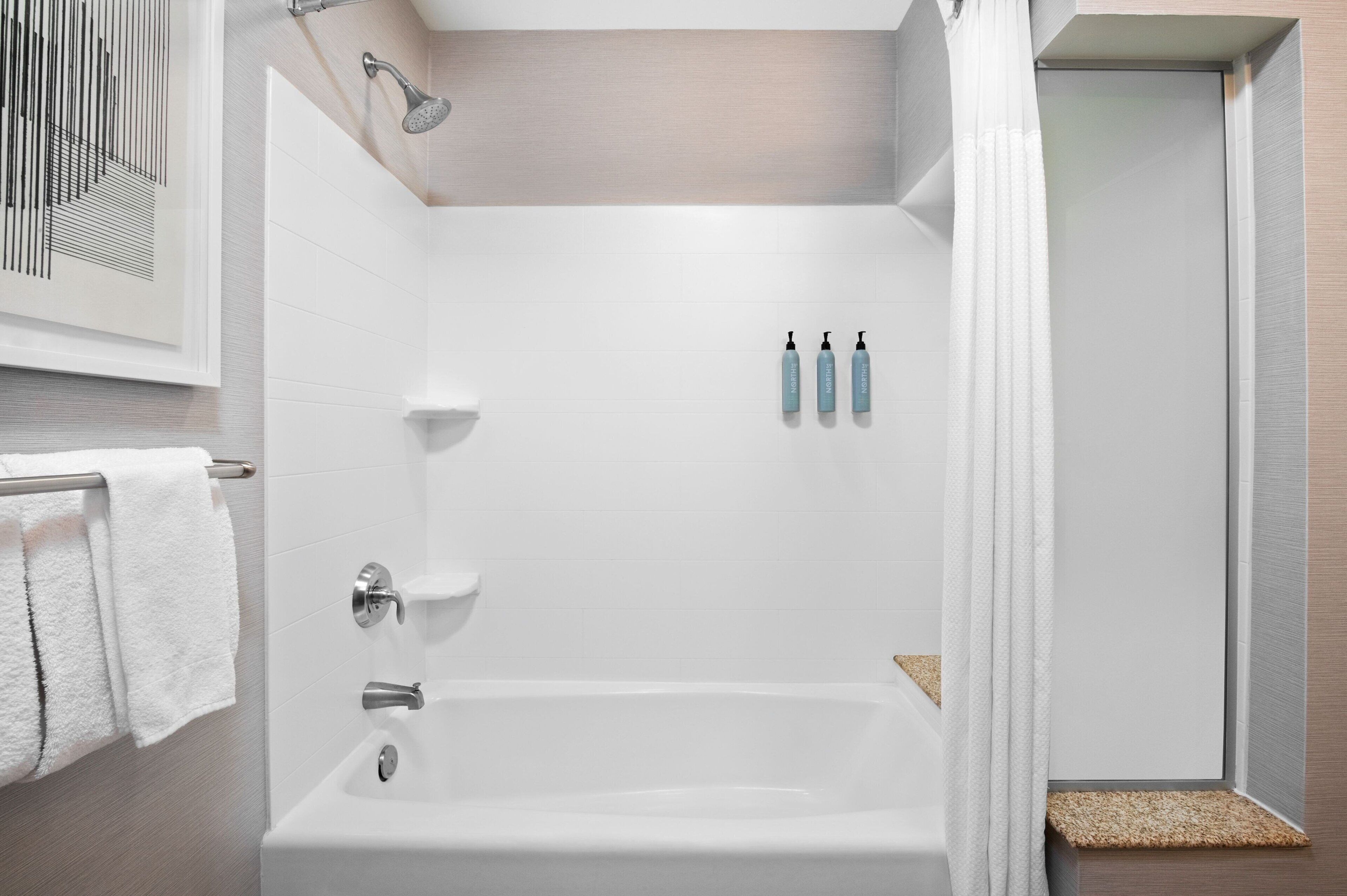 Un bagno moderno con vasca, doccia e WC. Si notano tre flaconi di shampoo e balsamo a parete.