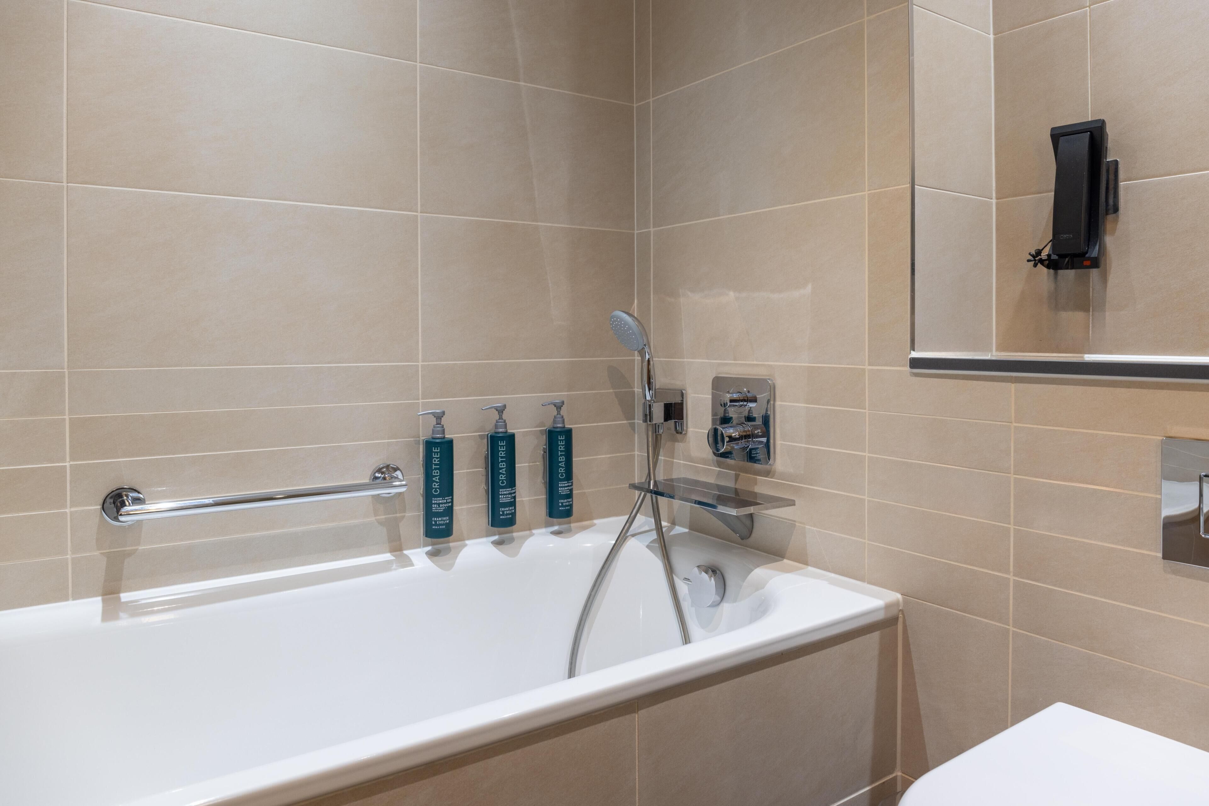 A modern bathroom with a bathtub, handheld showerhead, and three bottles of Crabtree body wash.