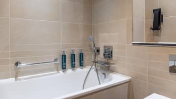 Un baño moderno con bañera, ducha de mano y tres botellas de jabón corporal Crabtree.