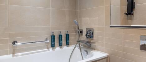 A modern bathroom with a bathtub, handheld showerhead, and three bottles of Crabtree body wash.