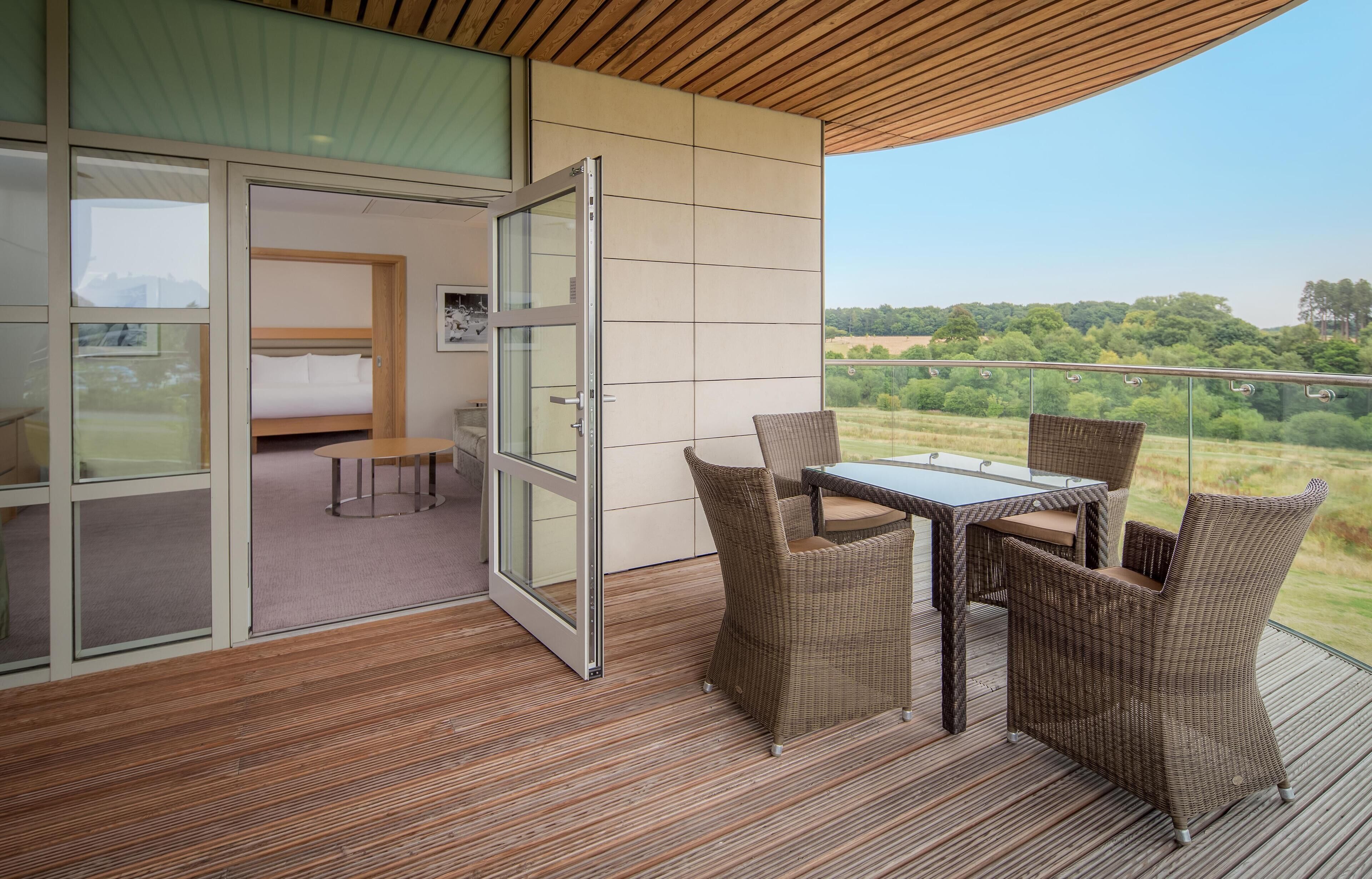 A balcony with wicker furniture, a glass door leading to a bedroom, and a view of the countryside.