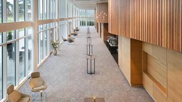 A corridor with chairs and tables, large windows, and wooden paneling.
