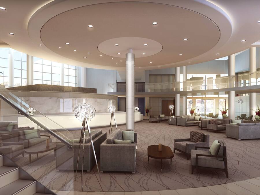A spacious lobby with a central column, seating areas, and a staircase.