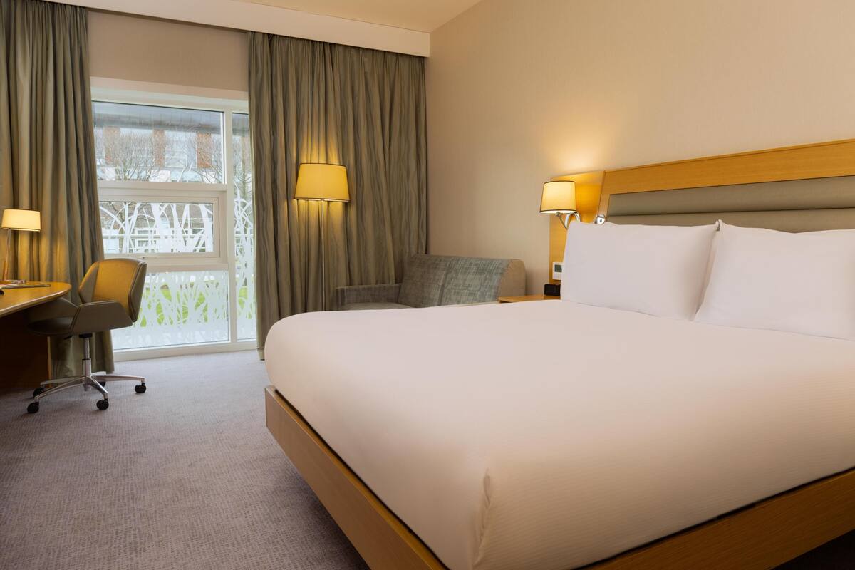 Une chambre d’hôtel avec un grand lit, un bureau, une chaise, deux lampes et une vue par la fenêtre.