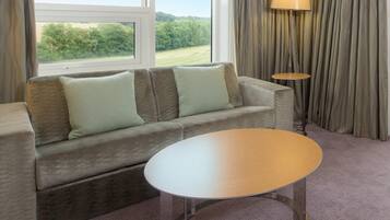 Una habitación con sofá, una mesa redonda, una lámpara y vistas al verdor a través de una ventana.