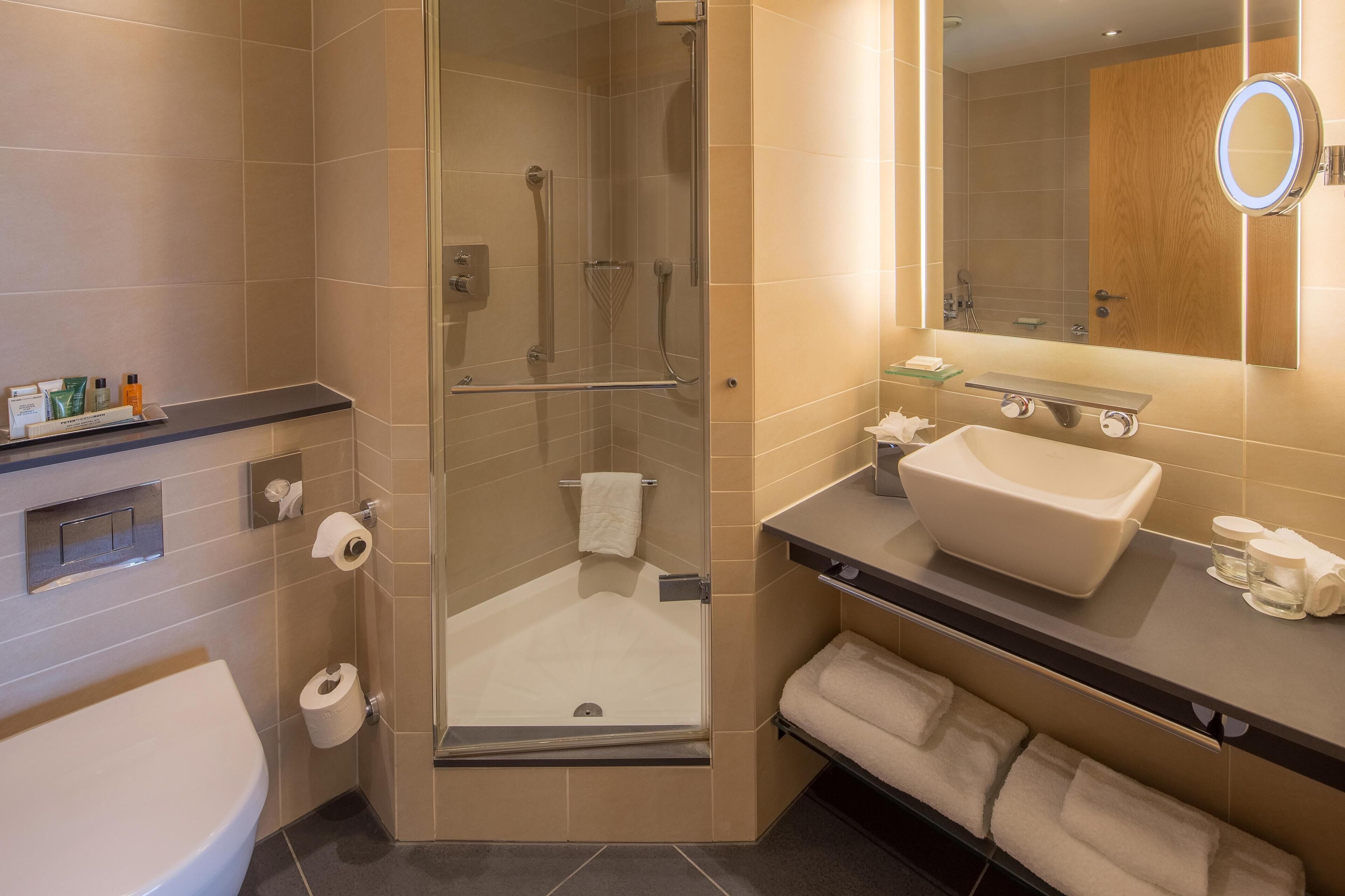 Un baño moderno con ducha de vidrio, lavabo amplio y tocador con espejo.