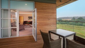 A balcony with a view of a green landscape, a table, and wicker chairs. - Hilton at St George's Park, Burton Upon Trent (Burton on Trent)