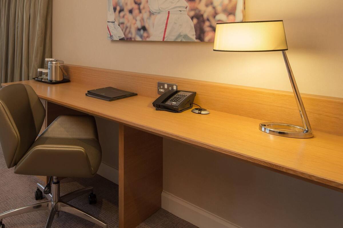Un bureau dans une chambre d’hôtel, avec une chaise, une lampe, un téléphone, une machine à café et un petit plateau avec une tasse et un verre.