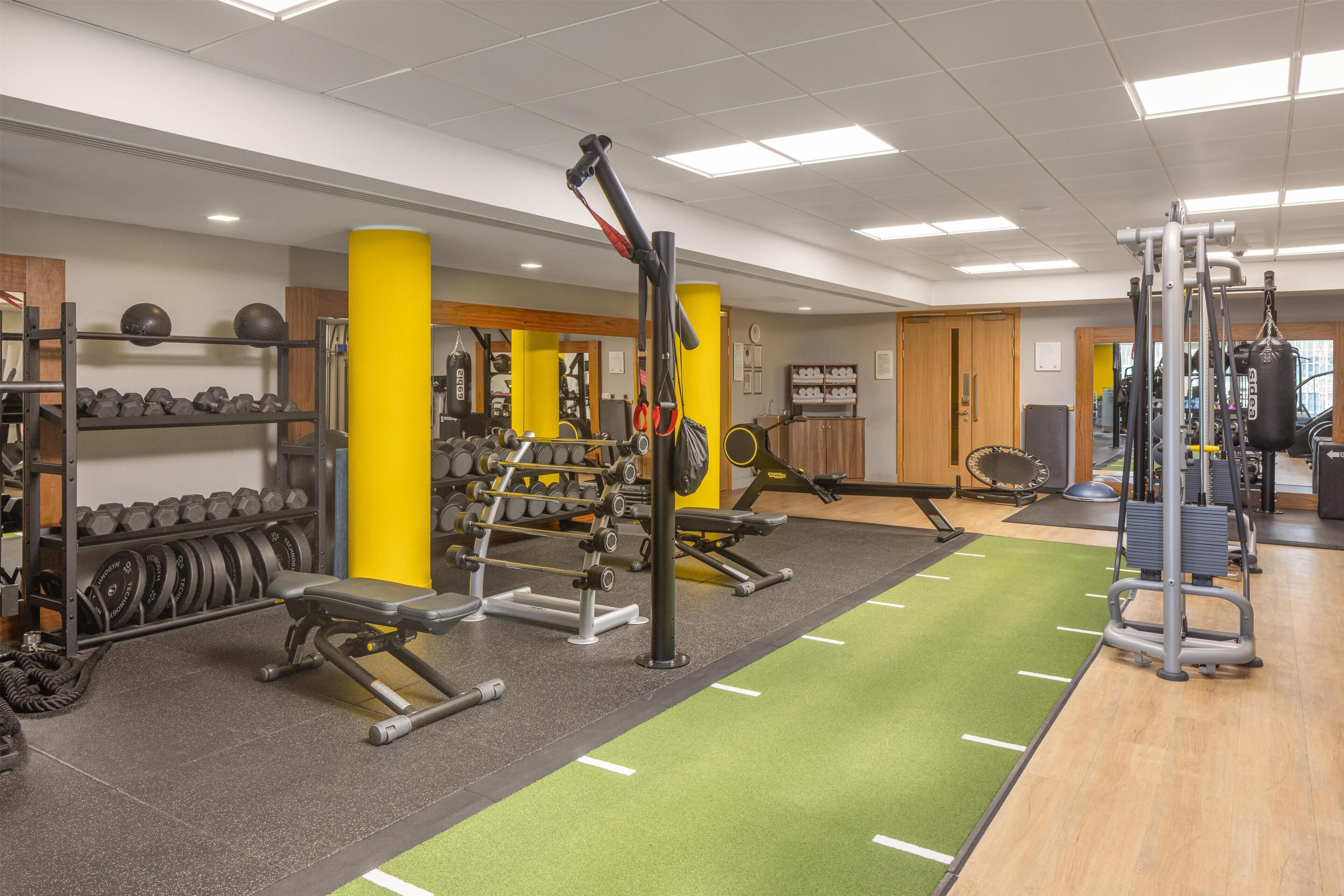 A gym with weightlifting equipment, a bench, and a green mat area.