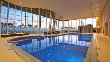 Une piscine intérieure dotée de parois en verre transparent, de chaises longues et d’un design architectural moderne.