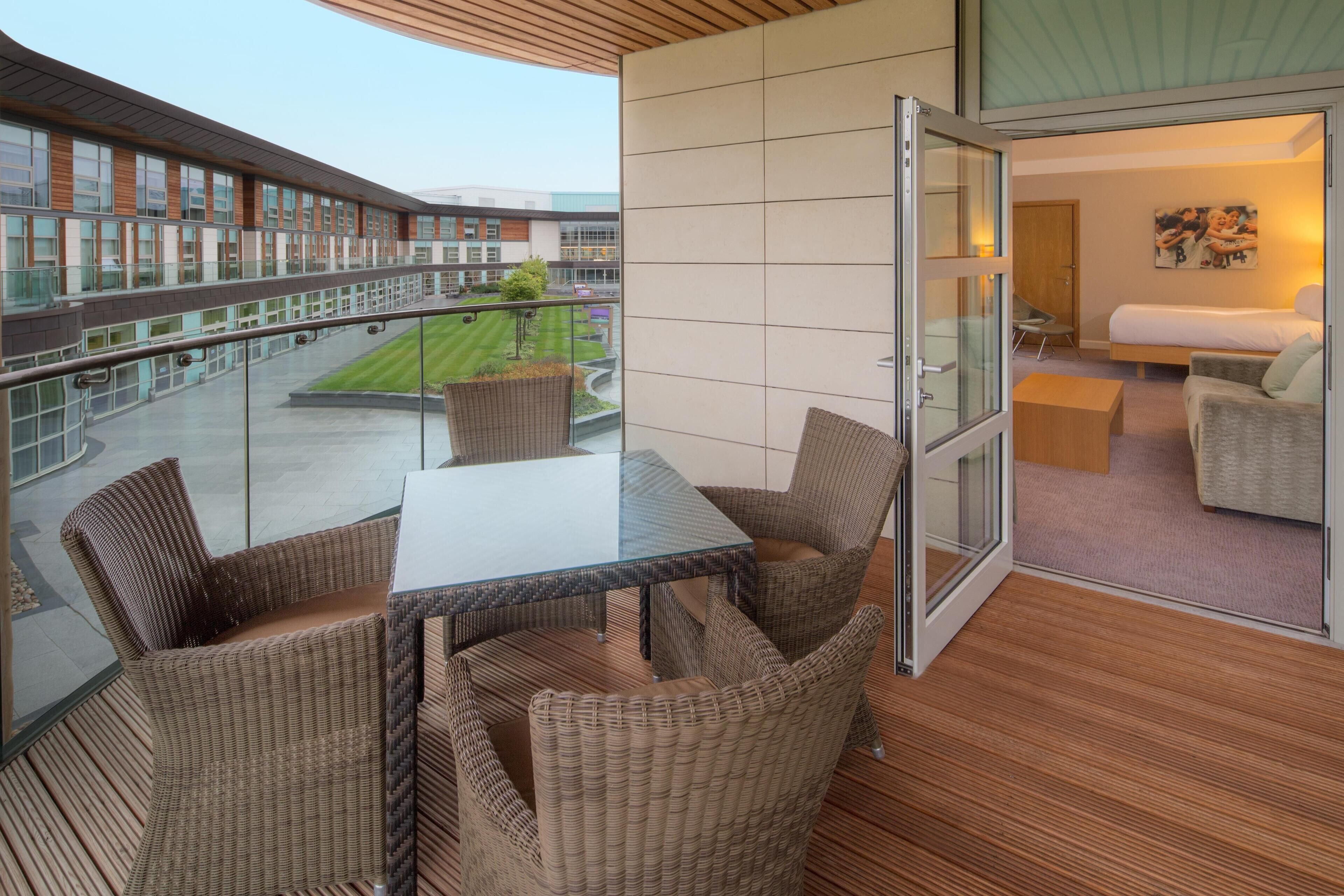 A balcony with wicker furniture, a glass table, and a view of a building complex.