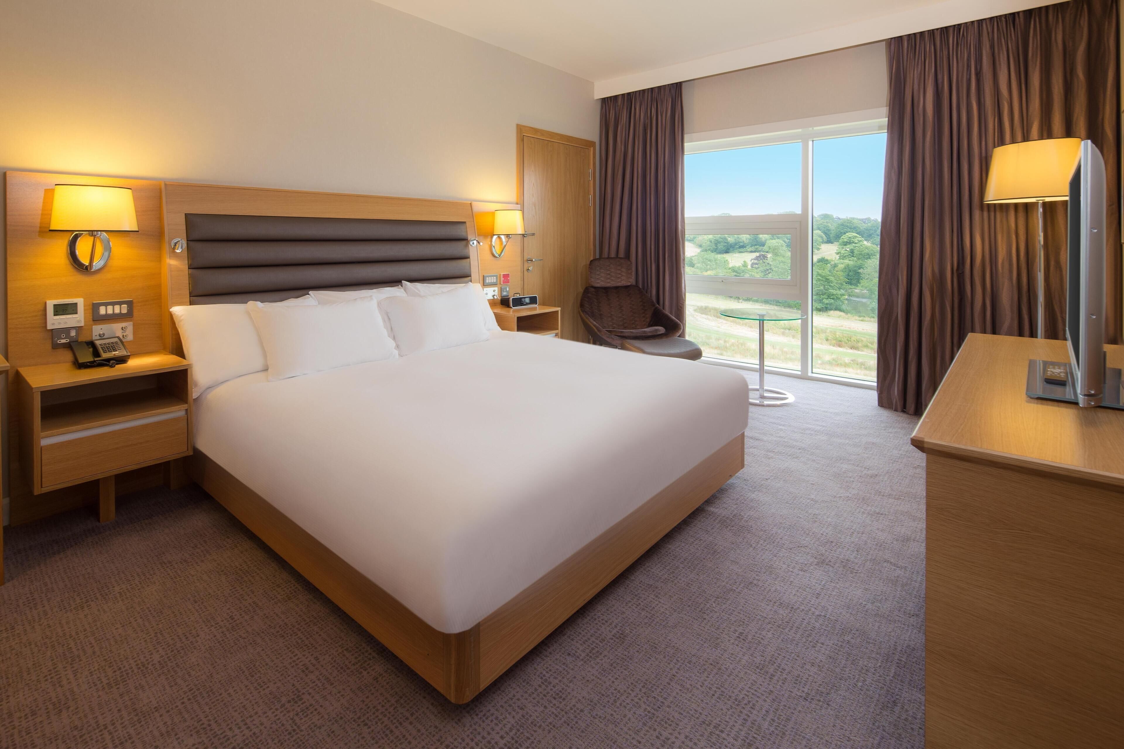 A hotel room with a large bed, bedside tables with lamps, a chair, a desk, and a view of the outdoors.