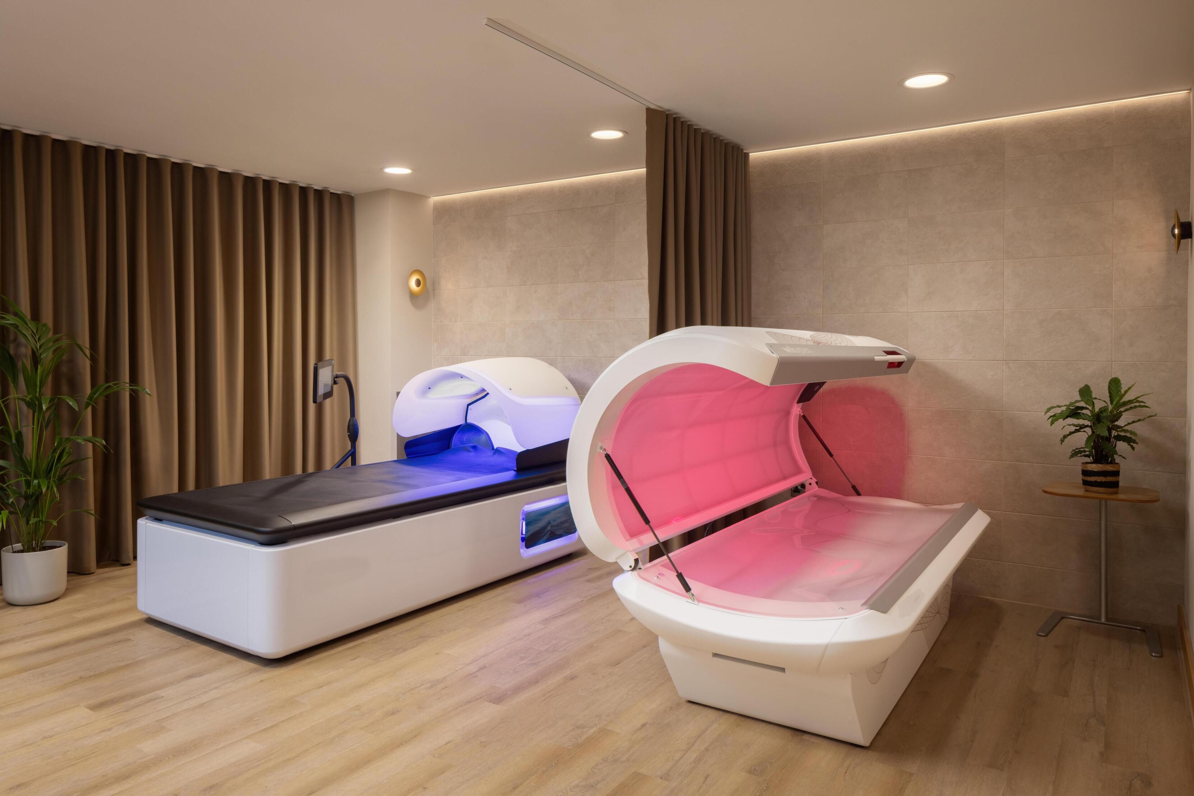 A room with a massage therapy bed, a small table with a plant, and a wall-mounted massage chair.