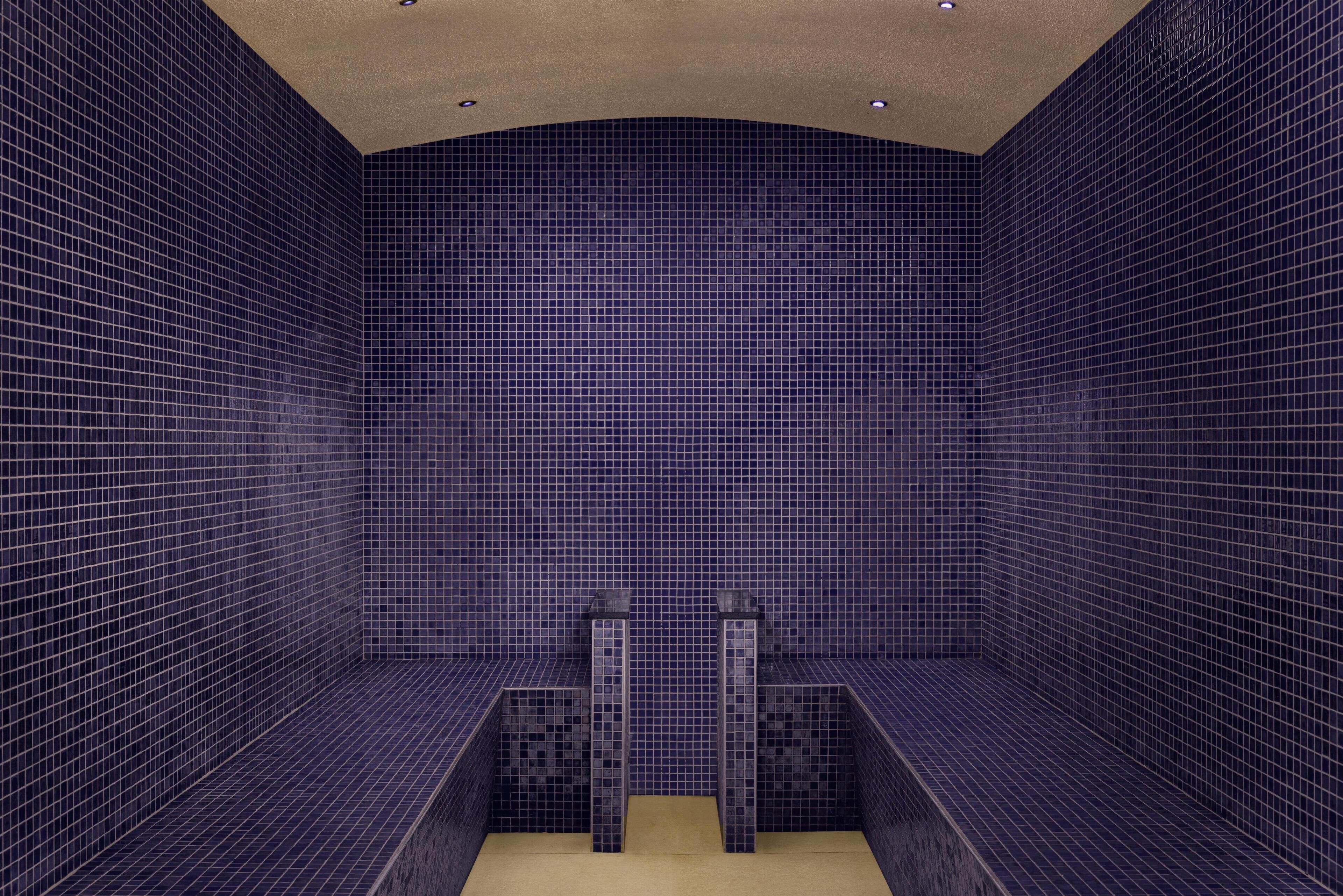 A room with dark blue tiled walls, a curved ceiling, and a central bench.