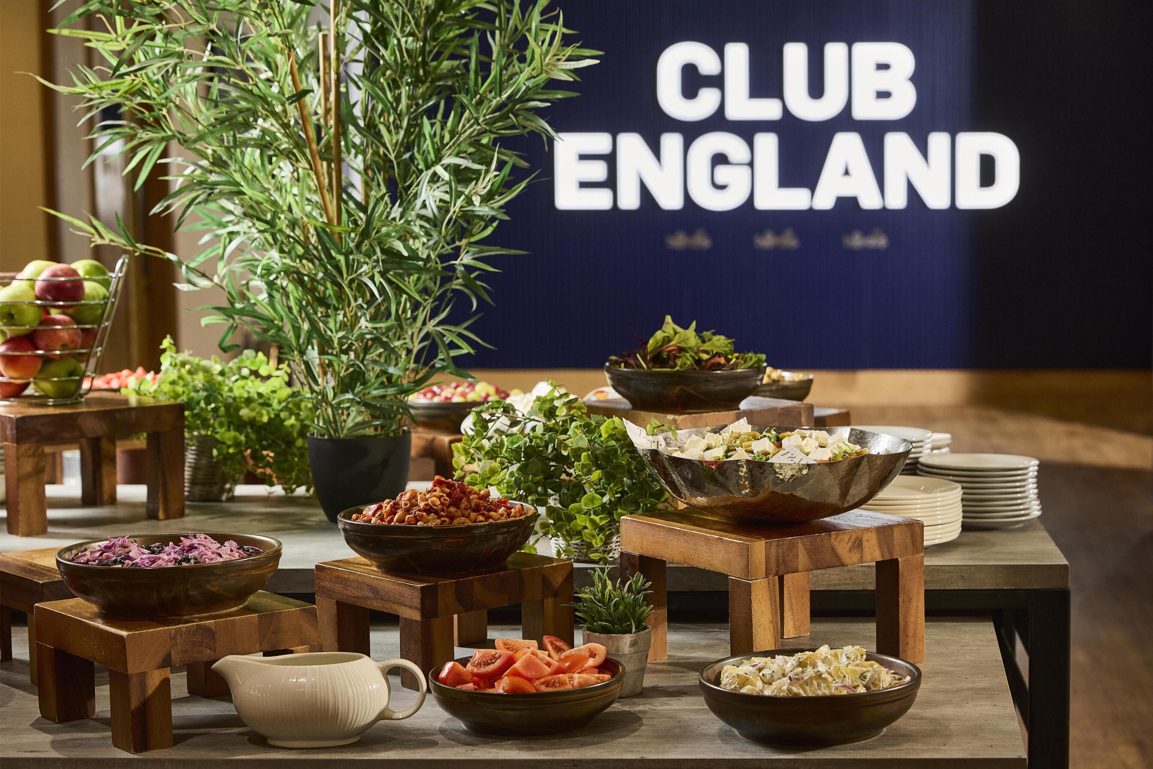 A buffet table with various dishes, a sign reading 'CLUB ENGLAND', and wooden furniture.