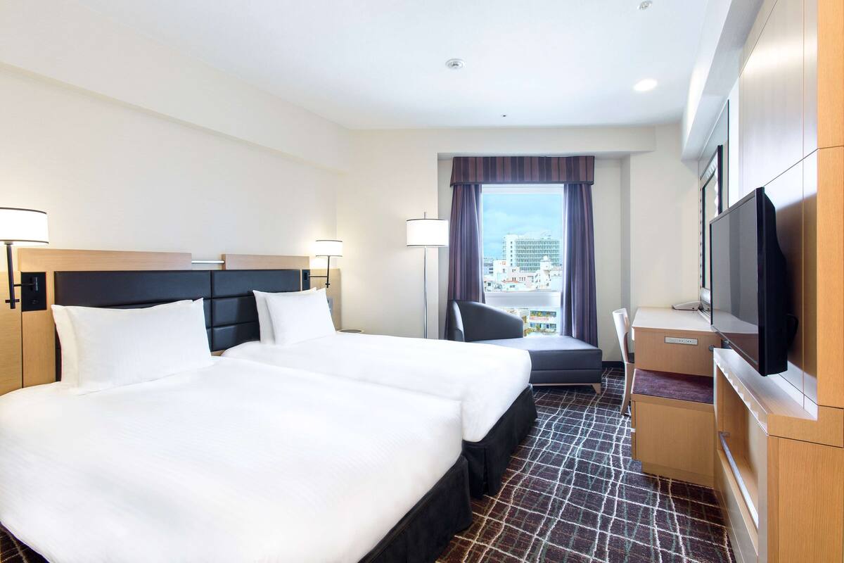 Habitación de hotel con una cama grande, un escritorio, un televisor y una ventana con vista a la ciudad.