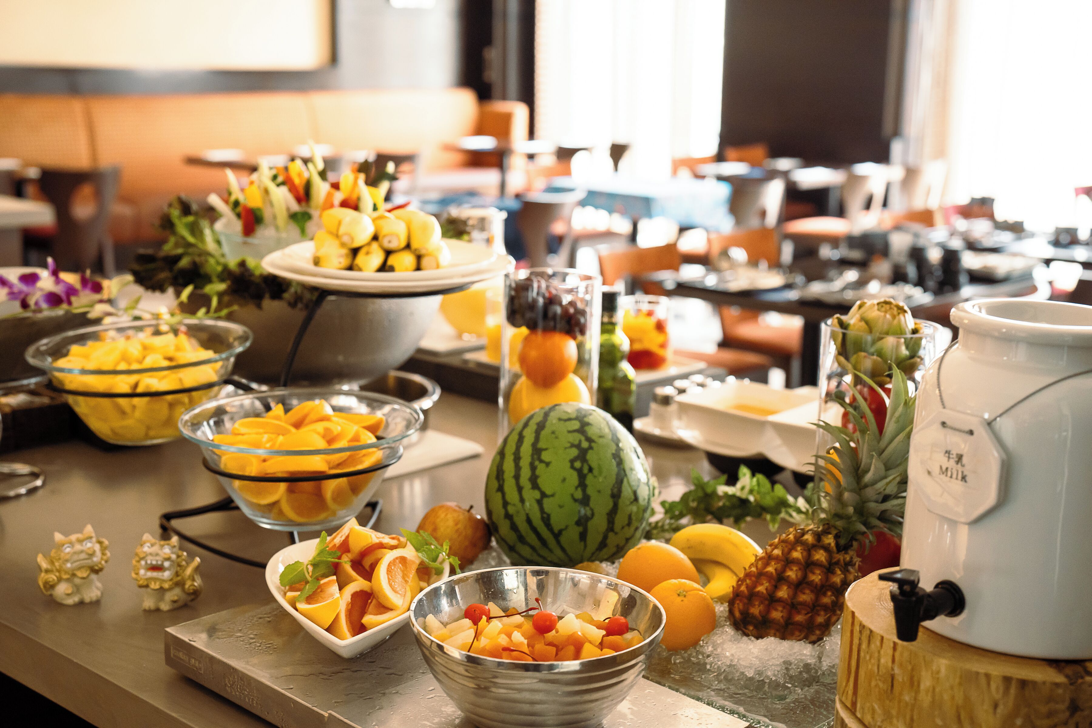 A buffet table with various fruits and a milk dispenser.