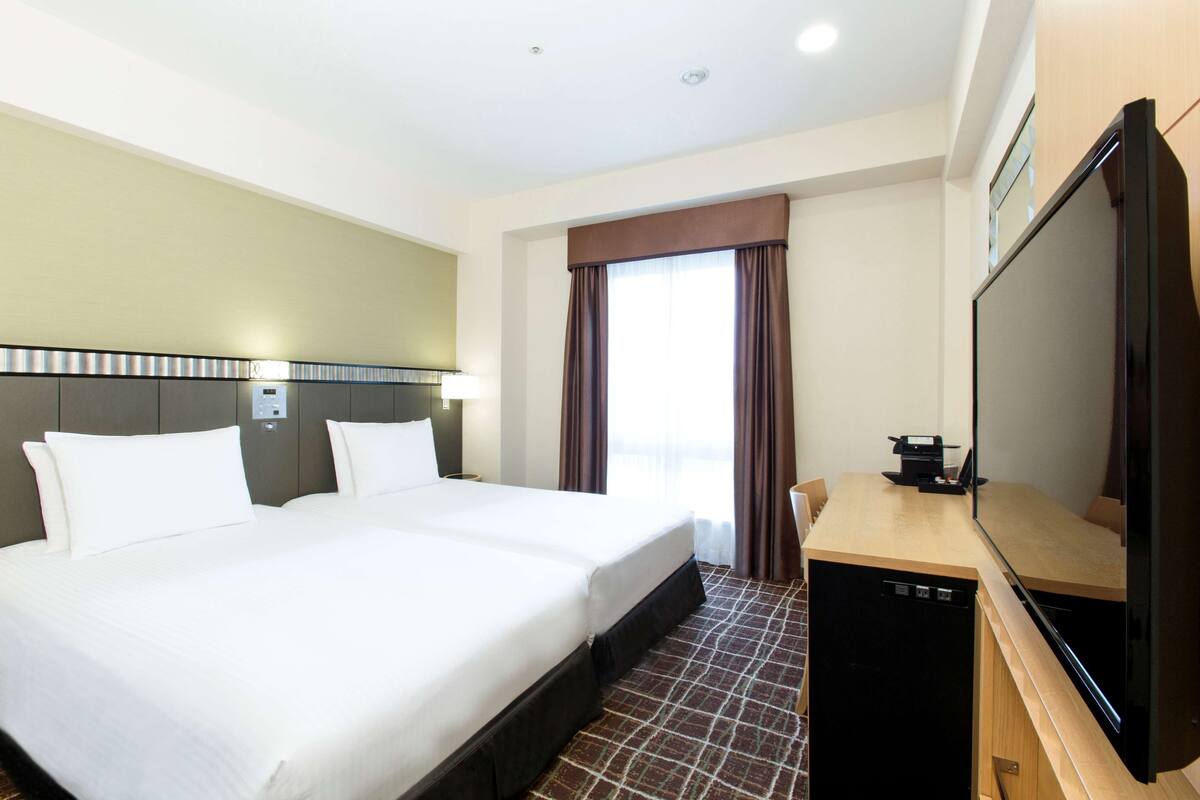 Habitación de hotel con una cama grande, un escritorio con televisor y una ventana con cortinas.