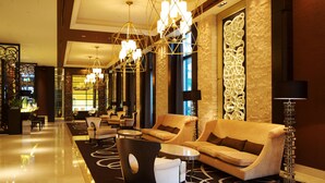 Un vestíbulo amplio con techo alto, candelabros modernos y una zona de estar con sofás y sillones.
