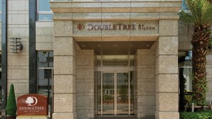 La entrada del hotel DoubleTree by Hilton, con fachada de piedra y una palmera cerca.