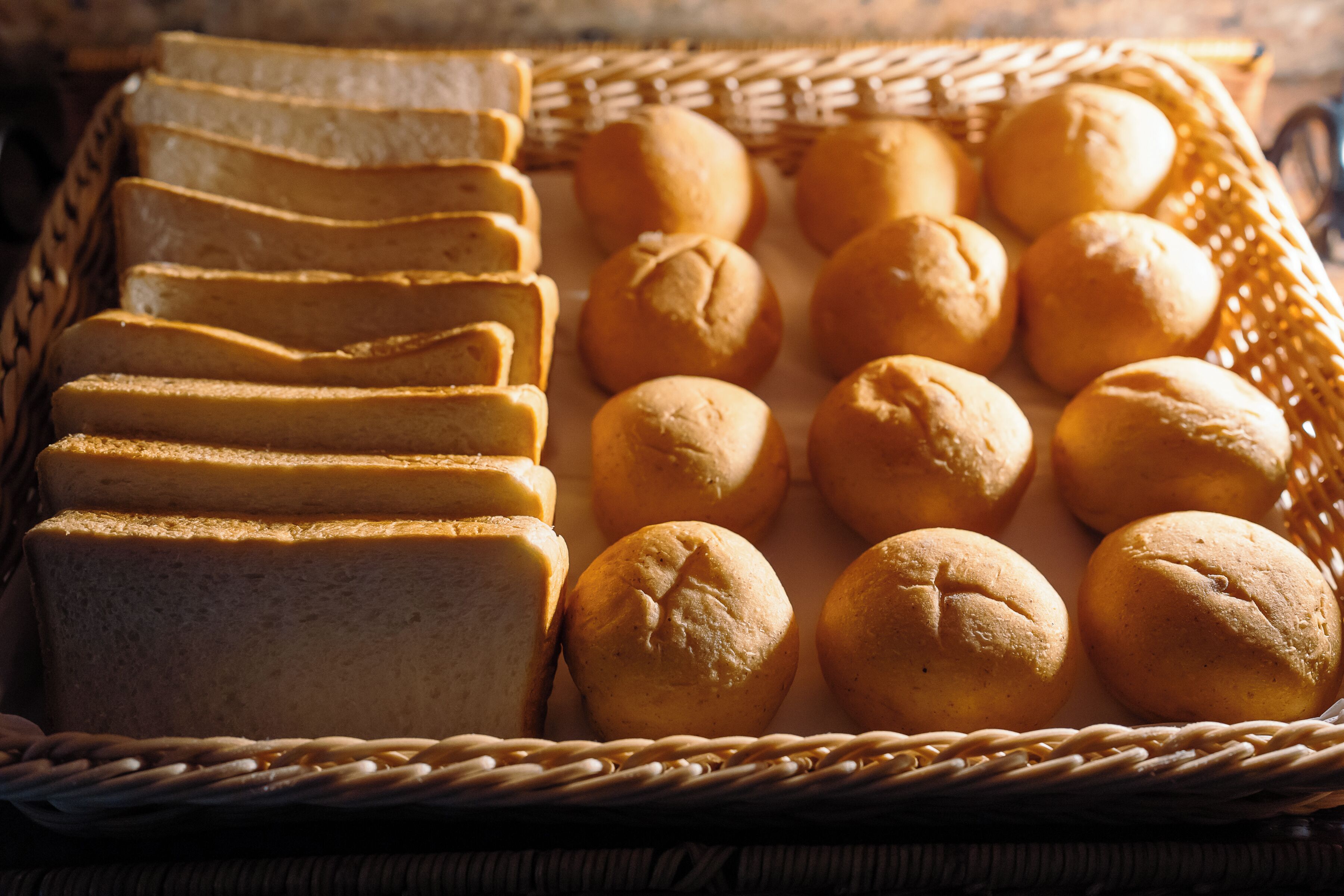 A basket containing sliced bread and round rolls.