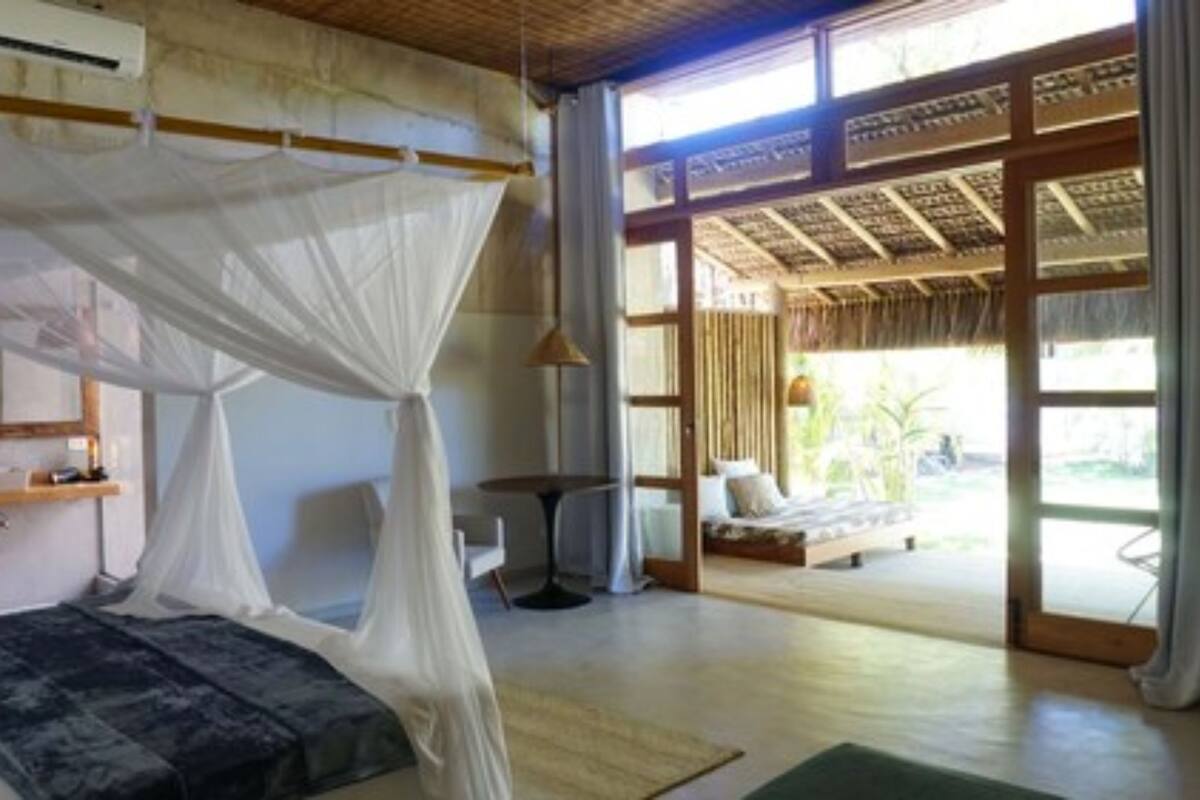 A room with a bed under a canopy, a small table, and a view of the outside.