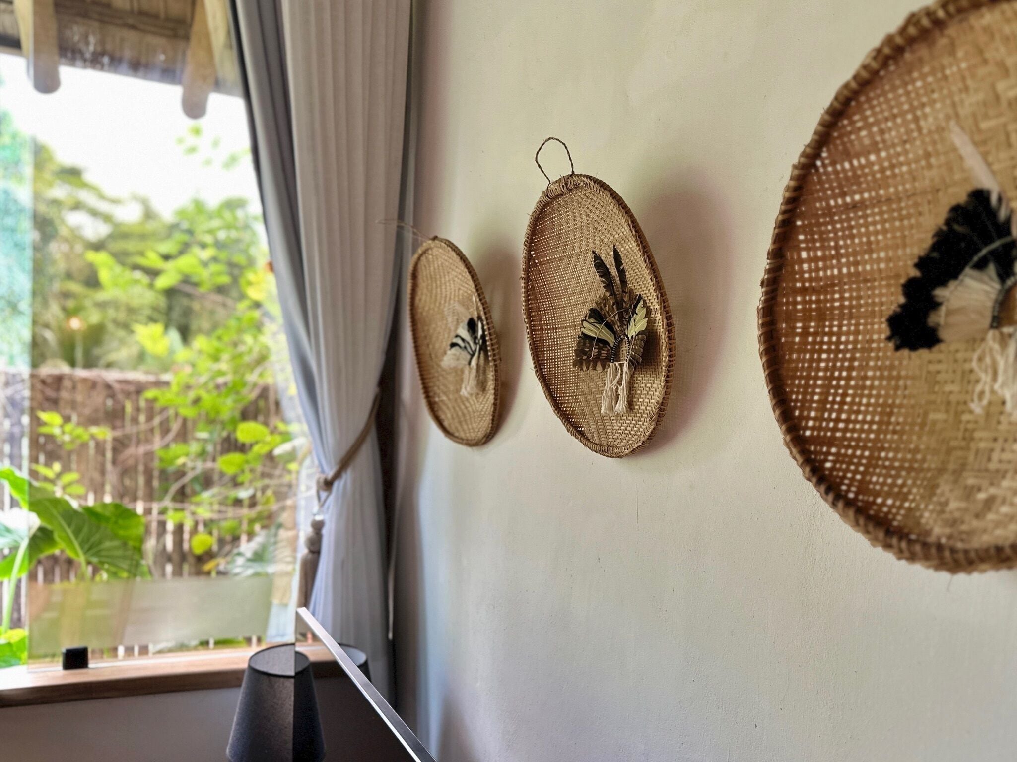 Tres tapices de pared tejidos con diseños de pájaros, una ventana con cortinas y vistas a zonas verdes al exterior.