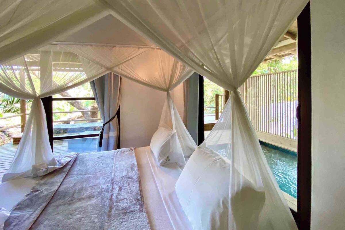A bedroom with a bed, white curtains, and a view of a pool.