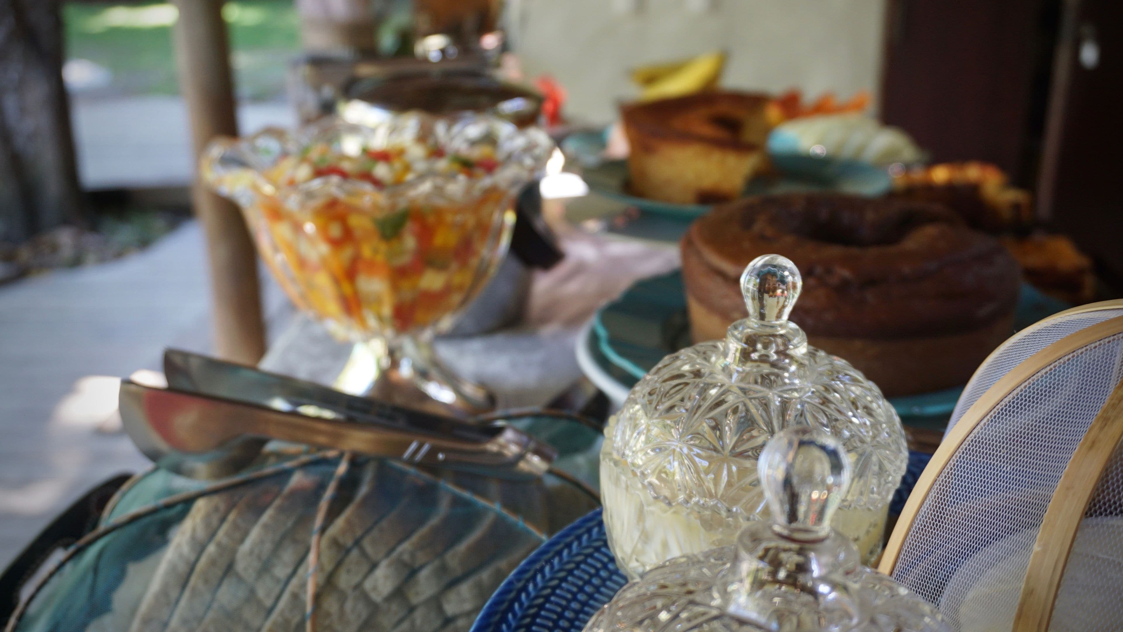 A table with various glassware and dishes, including a bowl of salad, a cake, and a covered container.