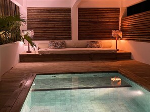 A modern indoor pool area with a wooden deck, a built-in seating area with cushions, and a wall with horizontal wooden slats. - Soleluna Casa Pousada (Porto Seguro)