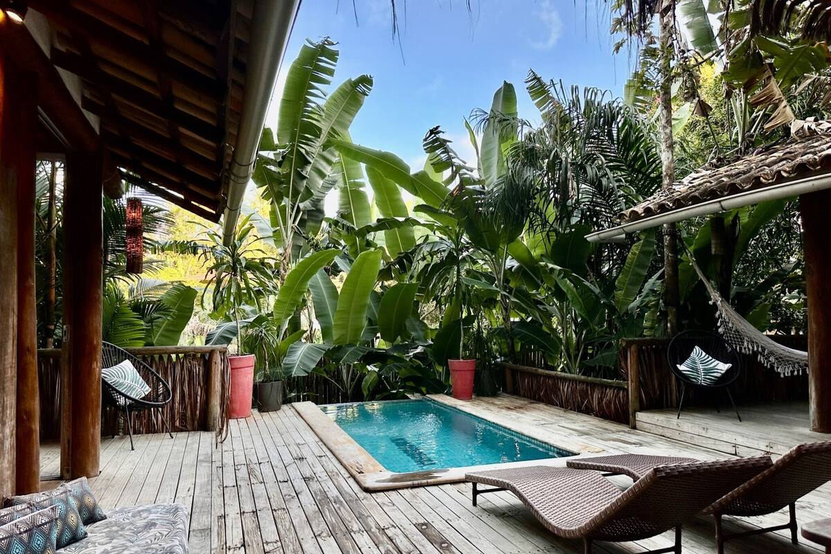 A wooden deck with a pool, lounge chairs, and tropical plants.