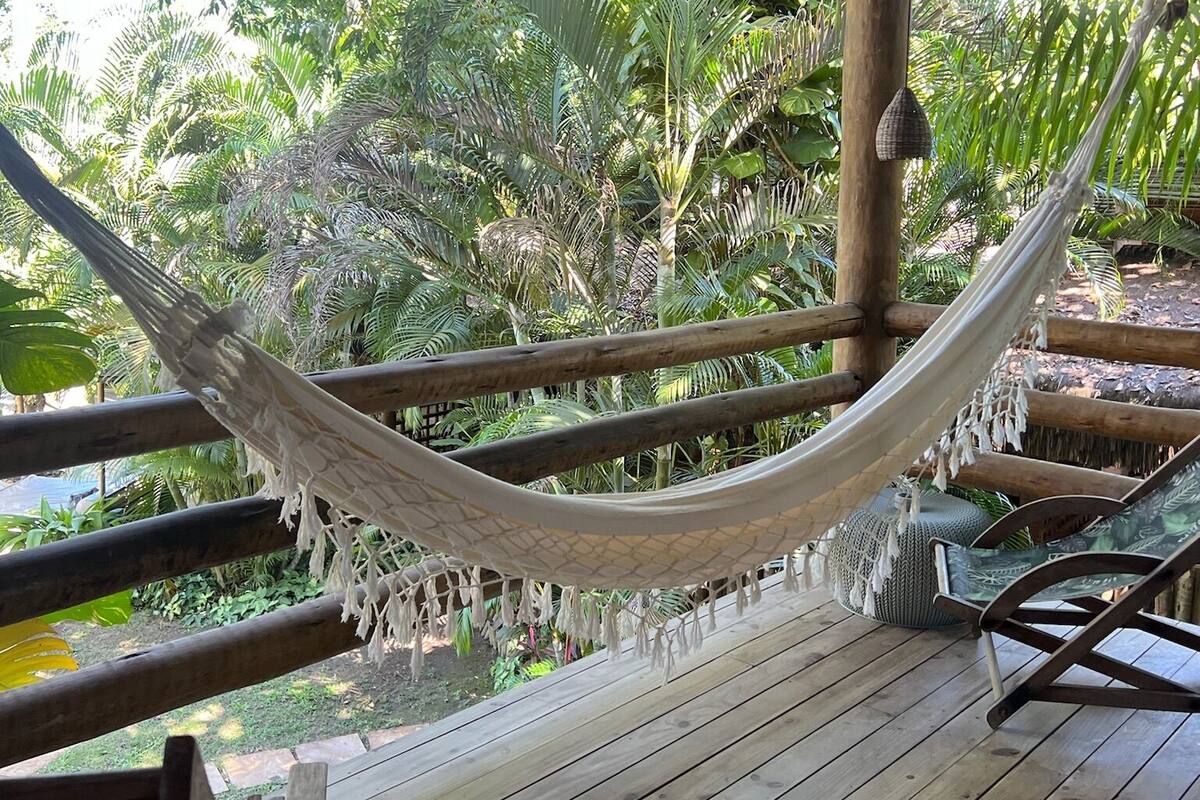 A hammock under a wooden pergola with a view of lush greenery.