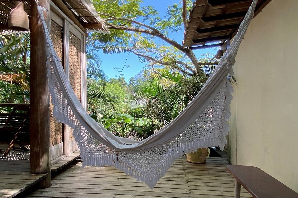 A hammock hanging between wooden pillars on a wooden deck with a view of tropical foliage.