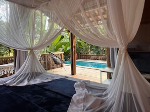 Ein Zimmer mit Pool, weißen Vorhängen, einem schwarzen Stuhl und einer Holzterrasse.