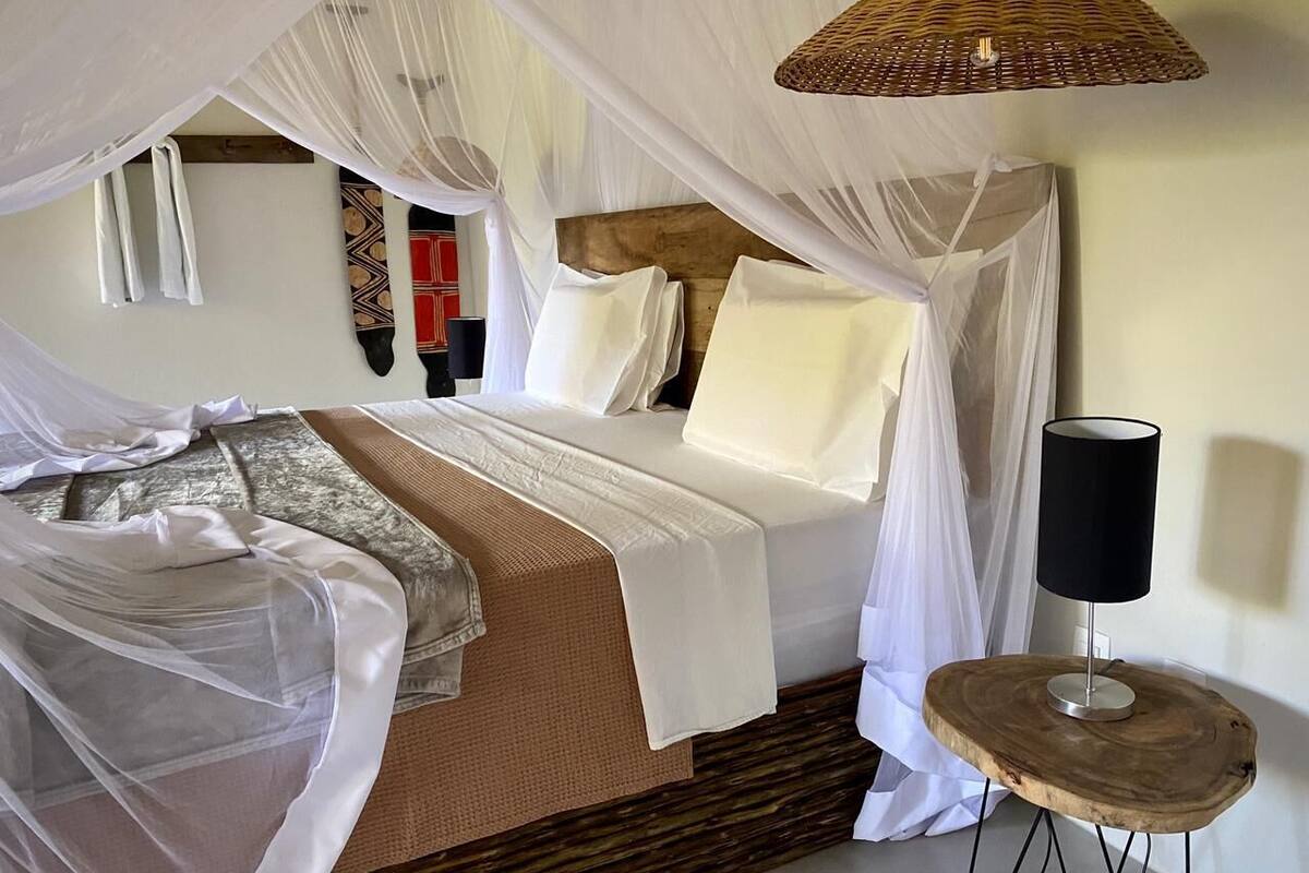 A bed with white bedding, a bedside lamp, and a woven basket on a round wooden table.