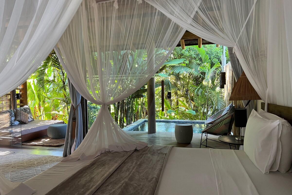 A bedroom with a canopy bed, a view of a pool, and lush greenery outside.