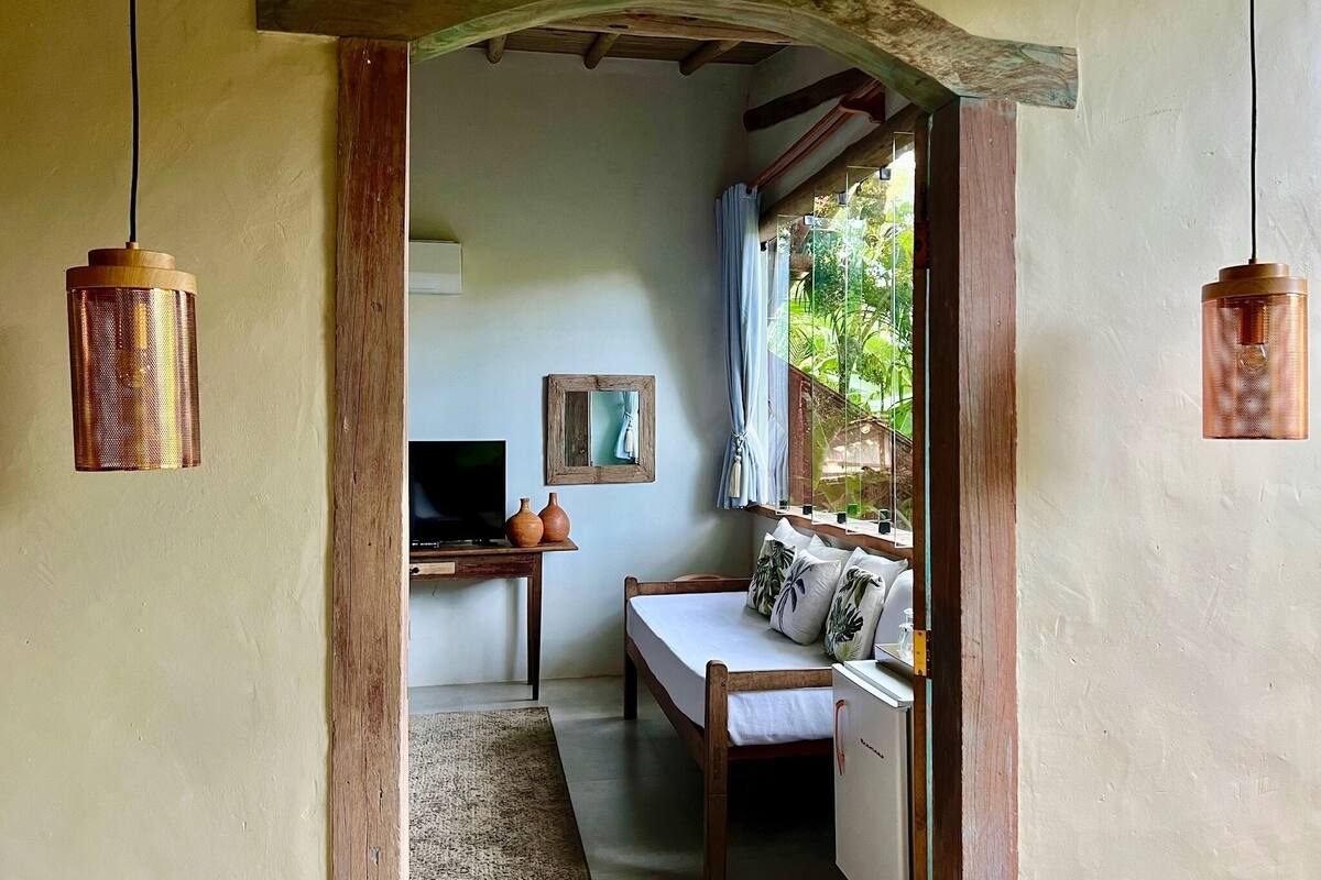 A cozy room with a wooden desk, a television, a sofa with cushions, and a window with curtains.