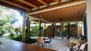 An open-air patio with a wooden ceiling, a patterned floor, and a seating area with chairs and a sofa. - Soleluna Casa Pousada (Porto Seguro)