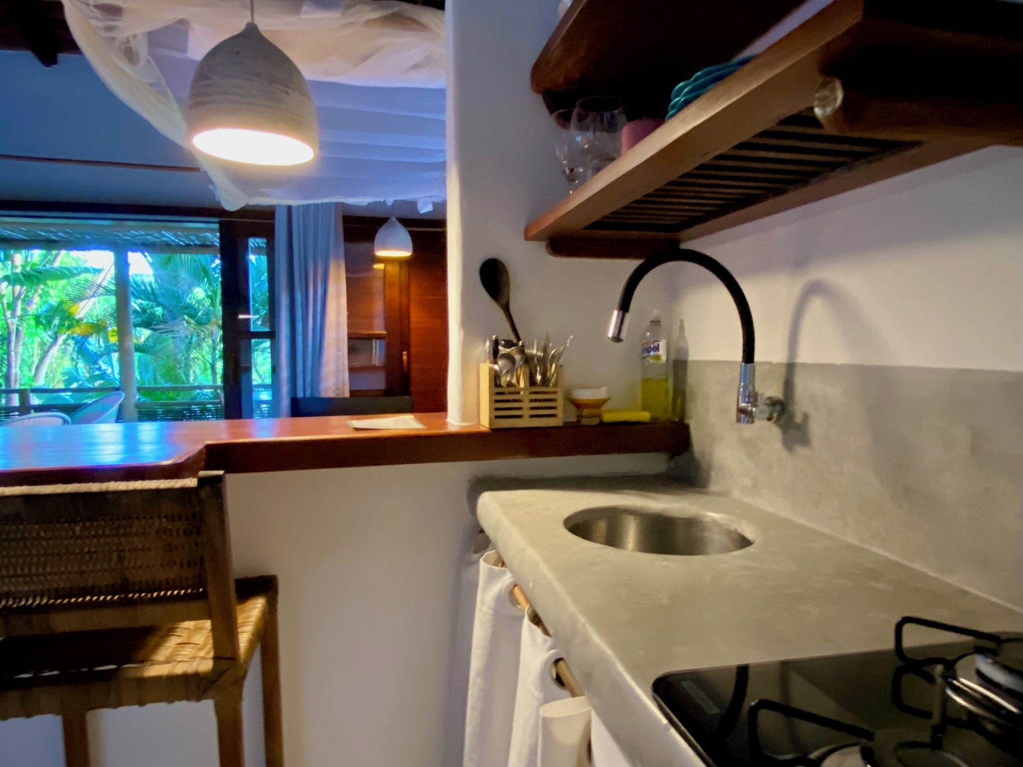 Une cuisine dotée d’un évier en acier inoxydable, d’un plan de travail en bois, d’un luminaire suspendu et offrant une vue sur la verdure à l’extérieur.