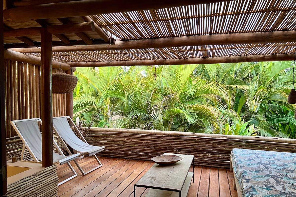 A wooden deck with two lounge chairs, a table, and a patterned sofa.